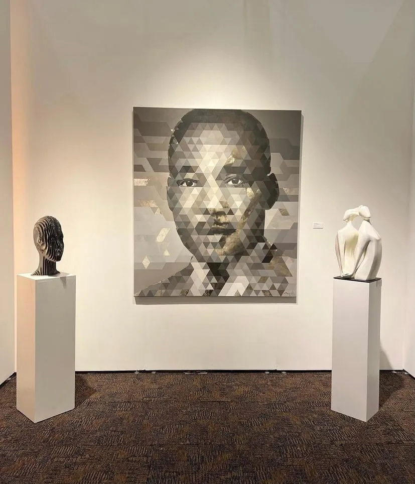 Art exhibition featuring a geometric portrait painting by Michael Azgour, flanked by two sculptural pieces on pedestals in a gallery setting.